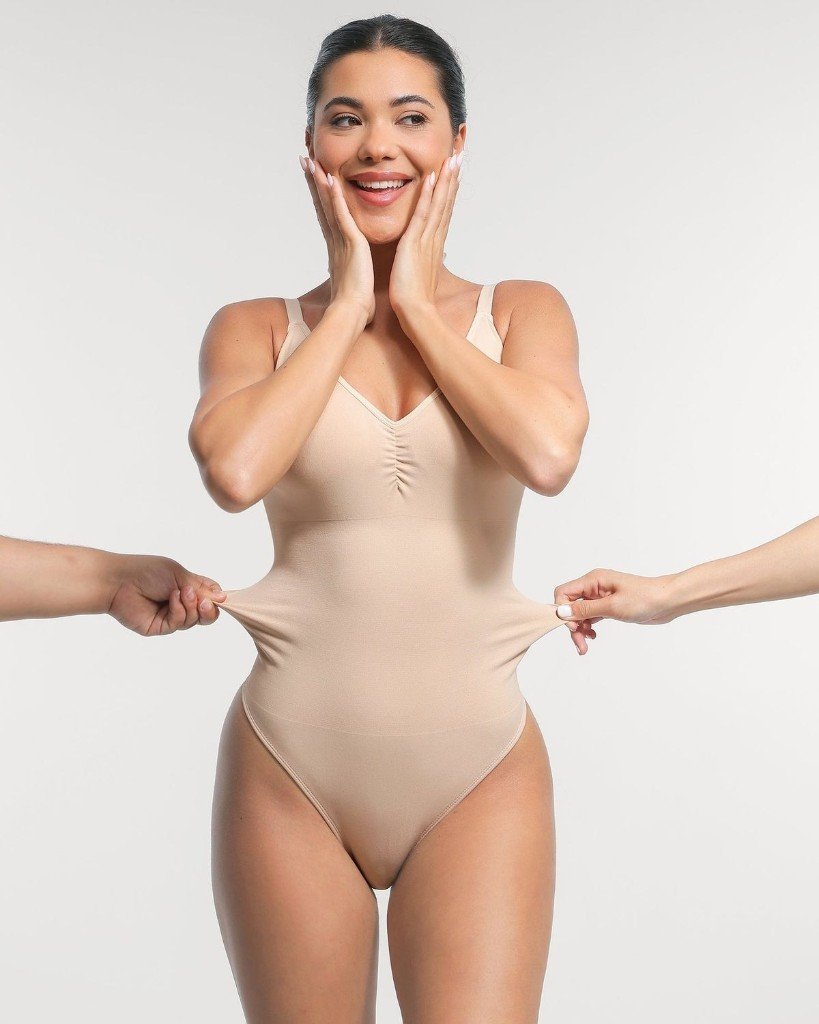 Smiling woman in a nude Jwear bodysuit showing fabric stretch